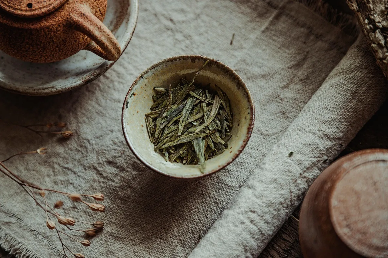 Platta gröna Longjing-blad i en liten skål bredvid en tekanna